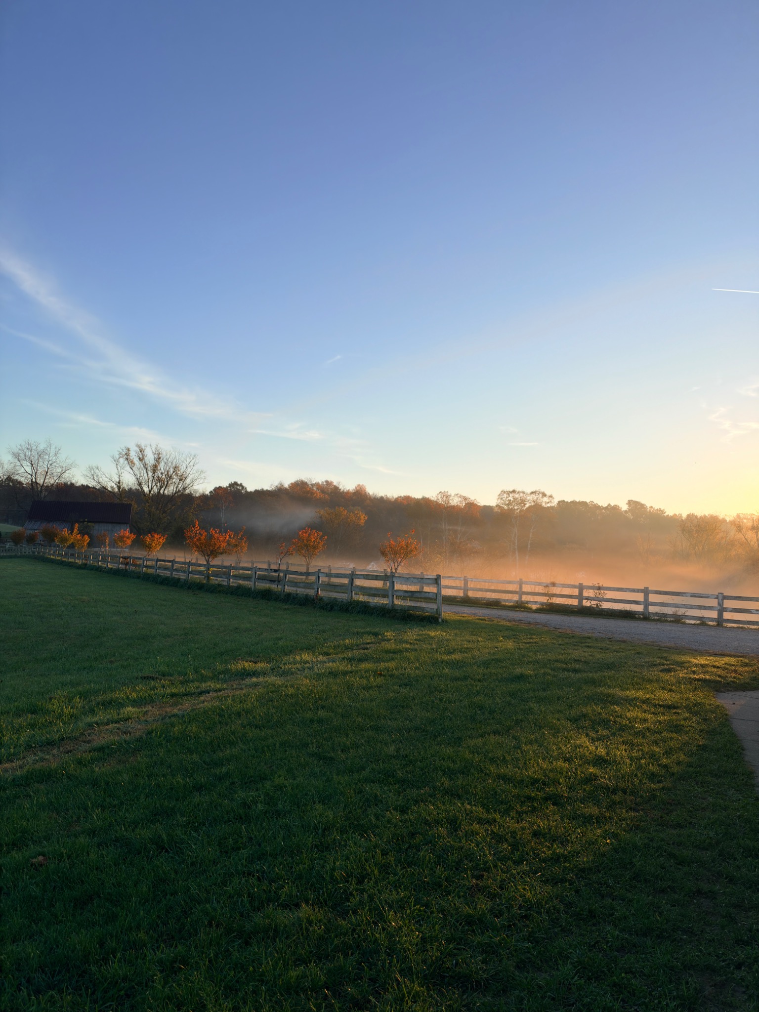 Morning mist over the Northbound meadow, with a fence and barn in the distance.